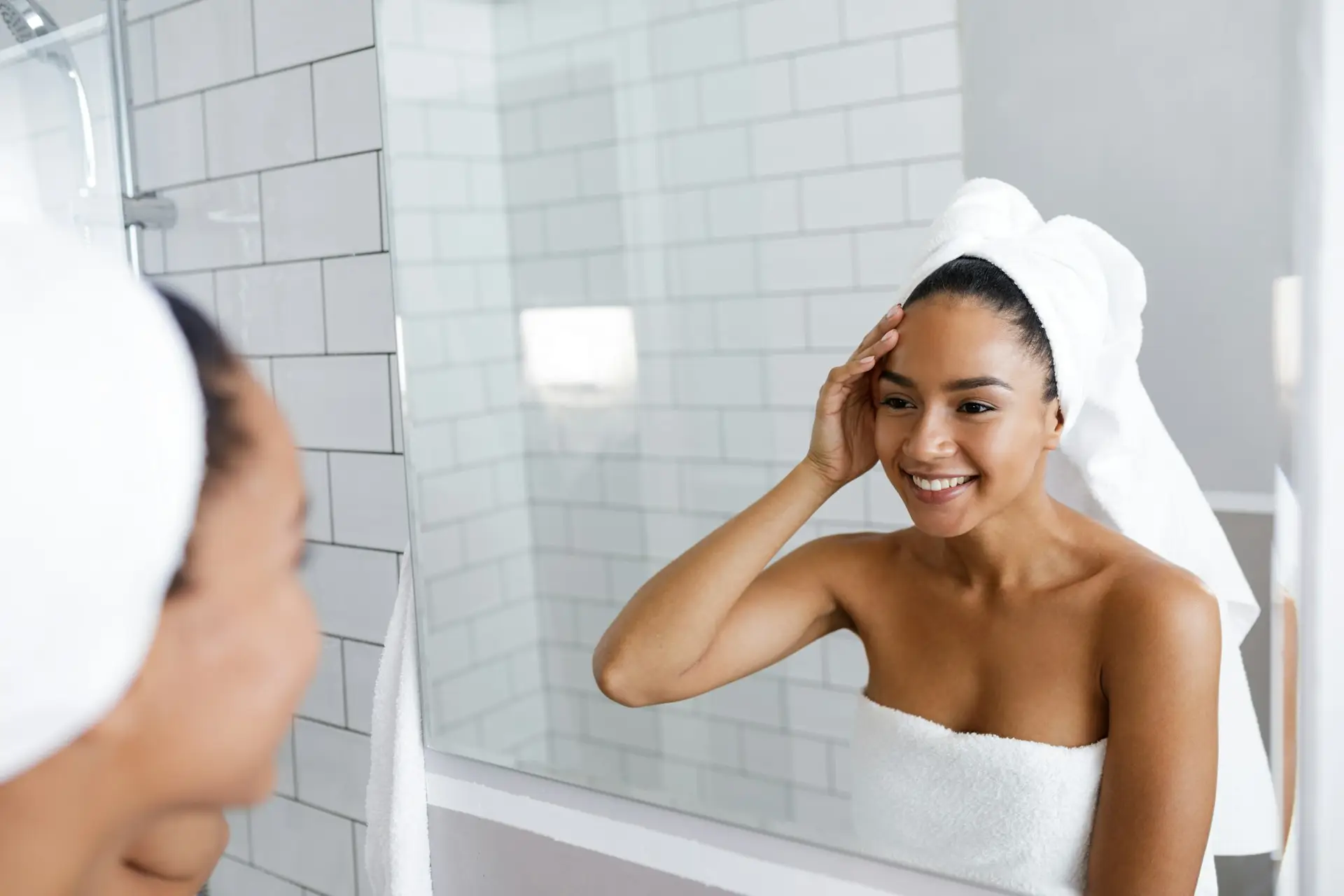 Beautiful young woman touching her skin while looking in the bathroom mirror